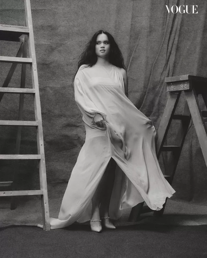Woman in flowing white gown posing between two wooden ladders for Vogue Philippines Make A Scene editorial