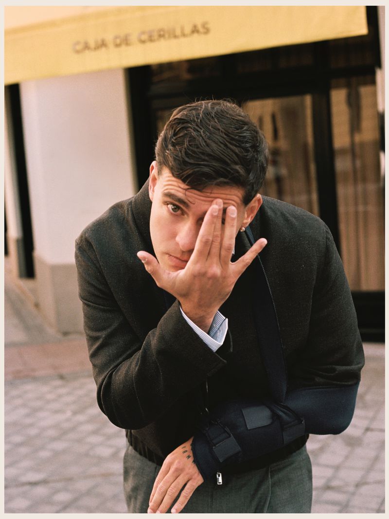 Man in dark jacket holding hand over his face outdoors on a street, photographed by Fede Delibes for Tapas Magazine.