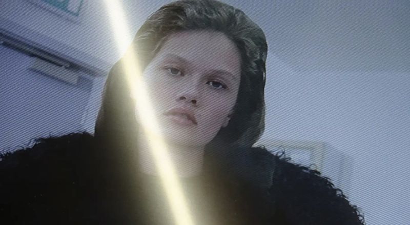 Portrait of a woman wearing a dark hooded jacket viewed through a screen with scan lines and a bright vertical light streak
