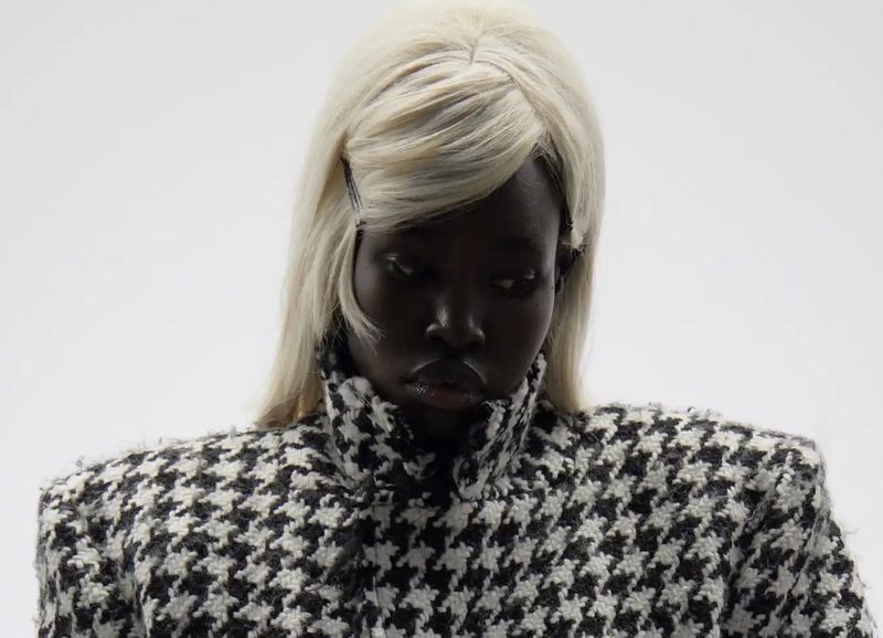 Portrait of a woman wearing a black and white houndstooth jacket and platinum blonde wig against a bright white background