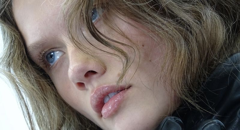 Close up portrait of a young woman with wavy brown hair and blue eyes wearing a black jacket for novembre global.
