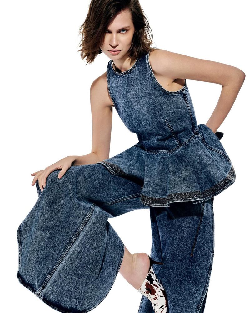Model wearing acid-wash denim sleeveless top and wide-leg trousers posing dynamically against a white background