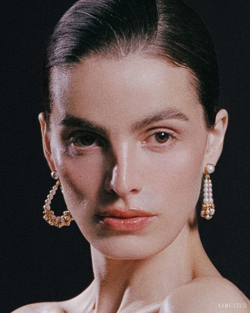 Close-up portrait of actor Lux Pascal wearing pearl drop earrings against a dark background for Coveteur.