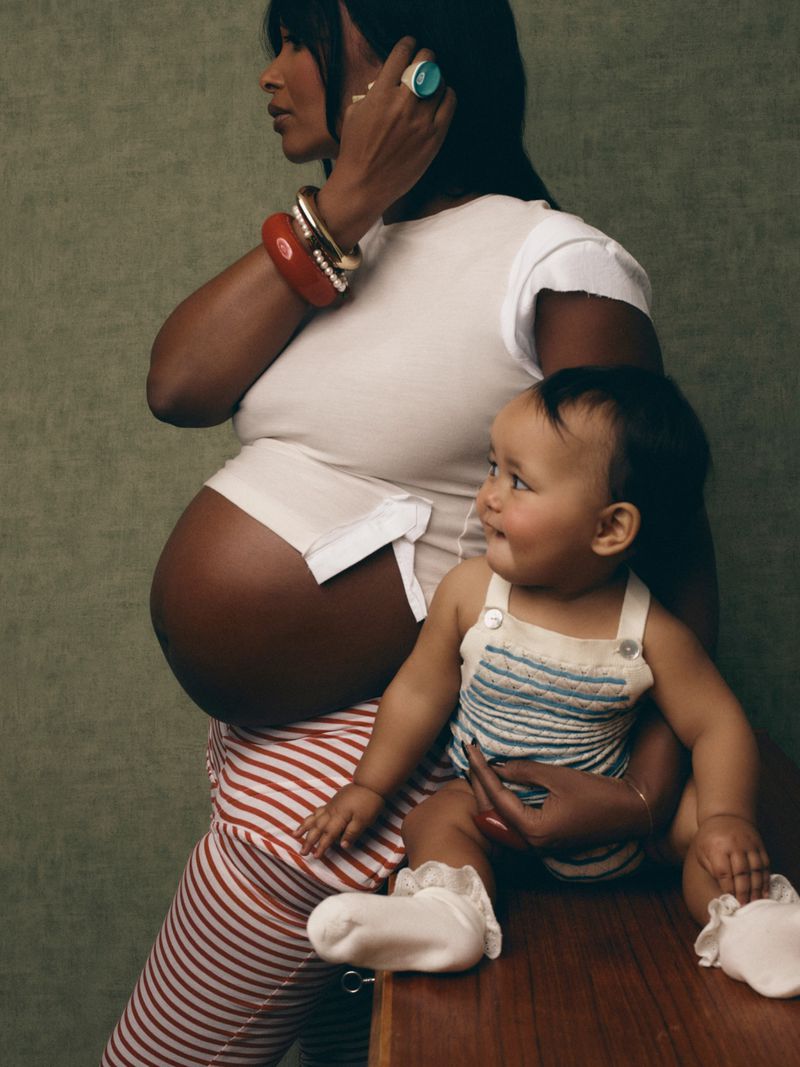 Pregnant woman wearing white t-shirt and striped pants holding toddler on a wooden surface against a textured green background
