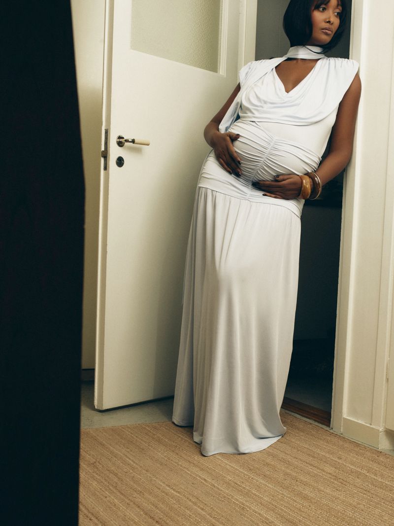 Pregnant woman wearing a white dress leaning against a door frame for Vogue Scandinavia by Illya Ovchar