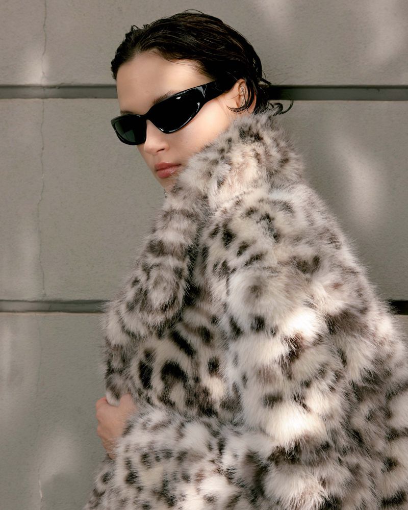 Model in black sunglasses wearing a fluffy animal-print coat against a grey wall for Harper's Bazaar Vietnam.