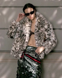 Model in leopard print coat and sequined skirt wearing sunglasses against a grey wall