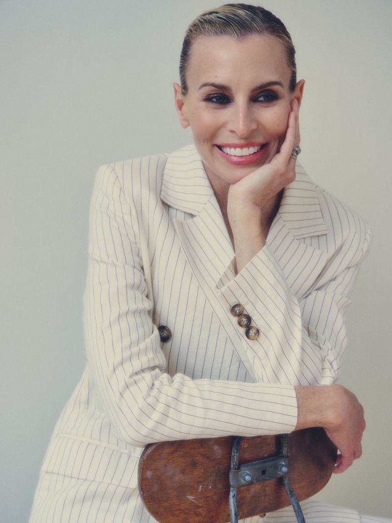 Portrait of model Niki Taylor wearing a pinstripe blazer resting her chin on her hand against a neutral background
