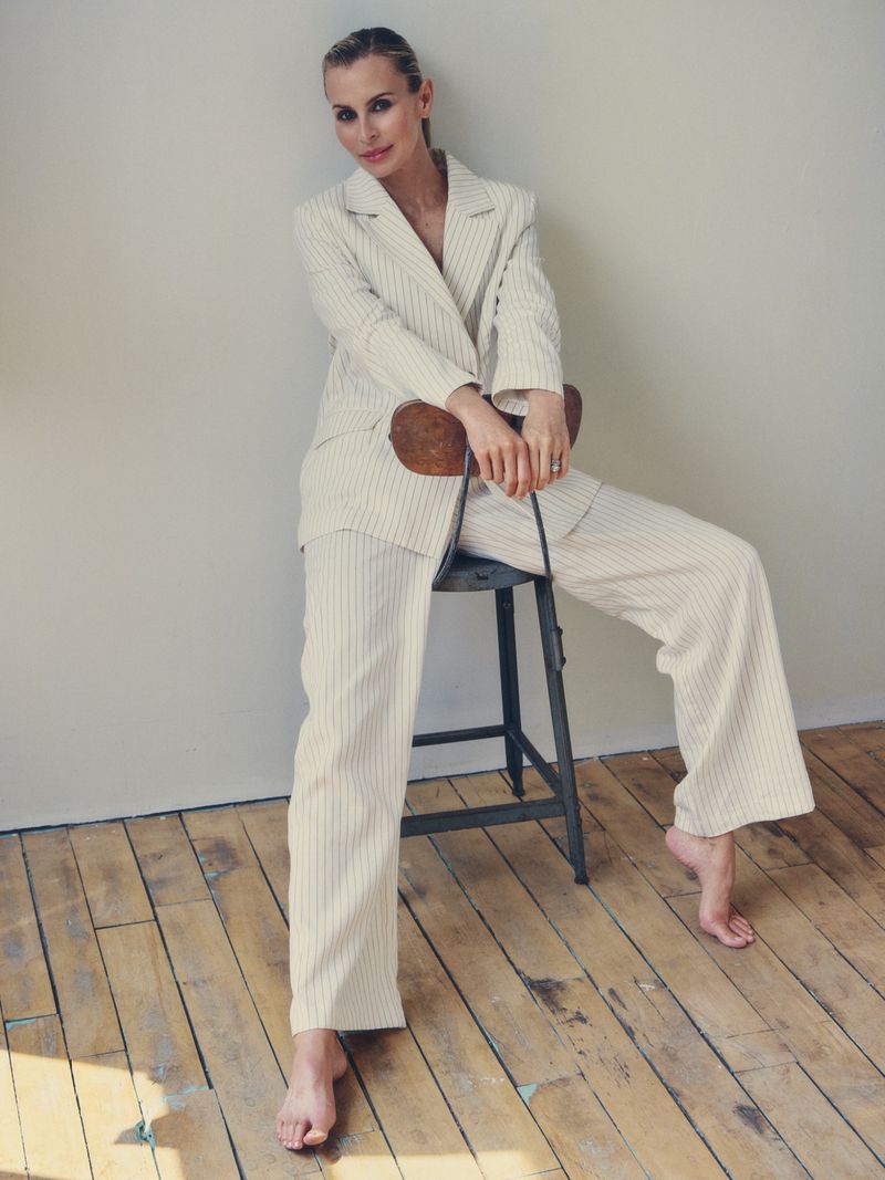 Model Niki Taylor sitting backwards on a metal stool wearing a cream pinstripe suit for Harper's Bazaar Australia.
