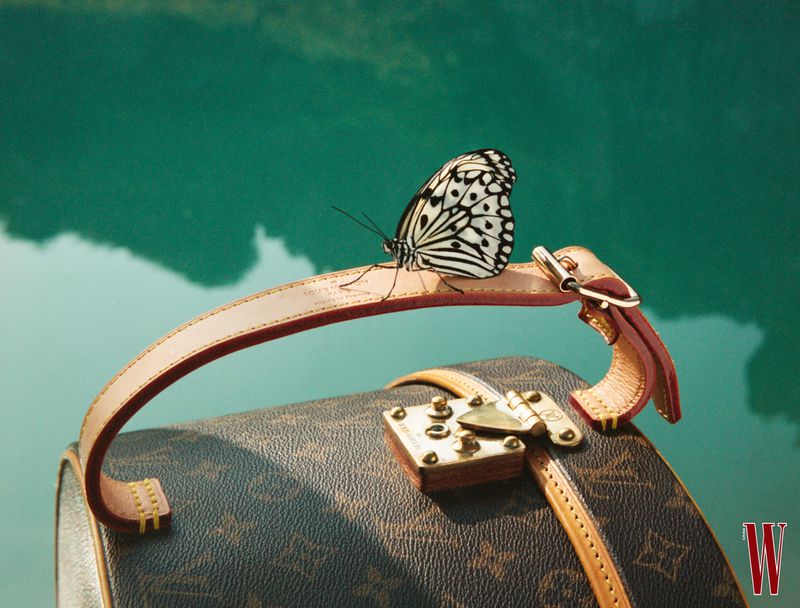 Close-up of a butterfly resting on the leather handle of a monogram vanity case against a teal water backdrop
