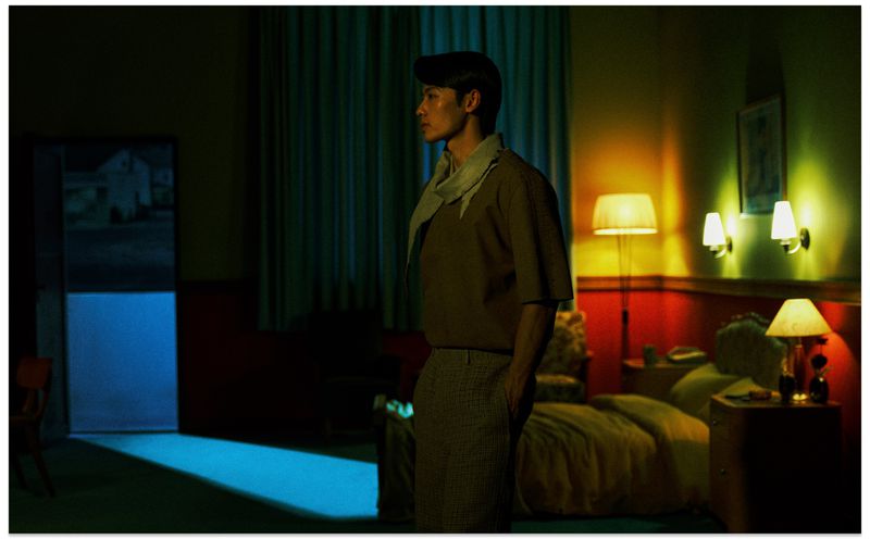 Profile of an Asian man standing in a dimly lit room with yellow lamps and a blue lit doorway in the background for Vogue China Men