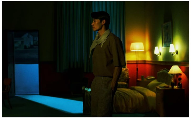 Profile of an Asian man standing in a dimly lit room with yellow lamps and a blue lit doorway in the background for Vogue China Men