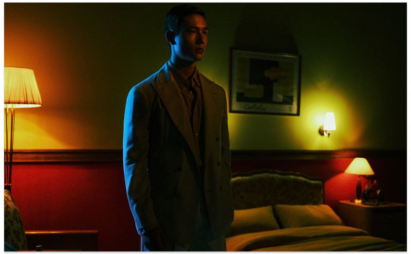 Man wearing a tailored suit standing in a dimly lit bedroom with warm lamps for Vogue China Men