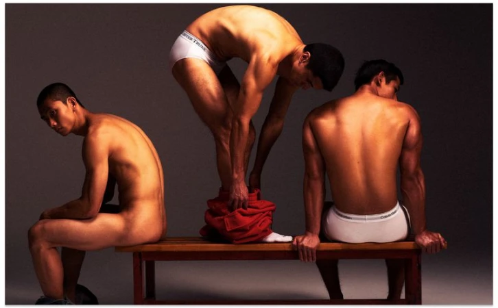 Three male models in white underwear on a wooden bench against a grey studio backdrop, photographed by Leslie Zhang for Vogue China Men.