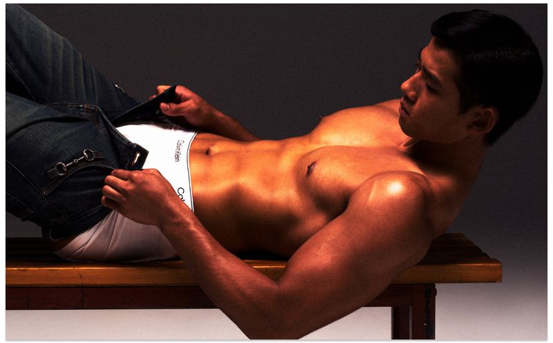 Shirtless man lying on wooden bench wearing white briefs and unbuttoned blue jeans for Vogue China Men