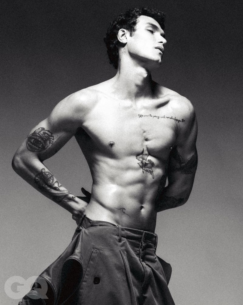 Monochrome portrait of a shirtless male model with tattoos posing against a grey backdrop for GQ Turkey