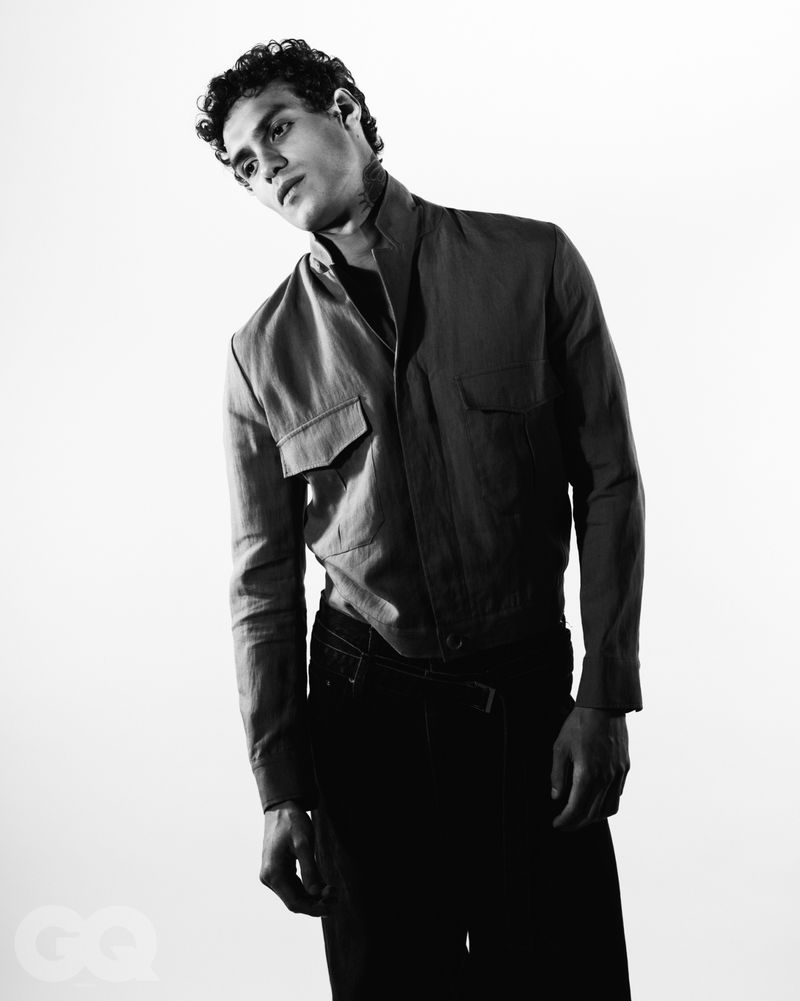 Black and white portrait of a male model wearing a button-up collared jacket against a plain white studio background.