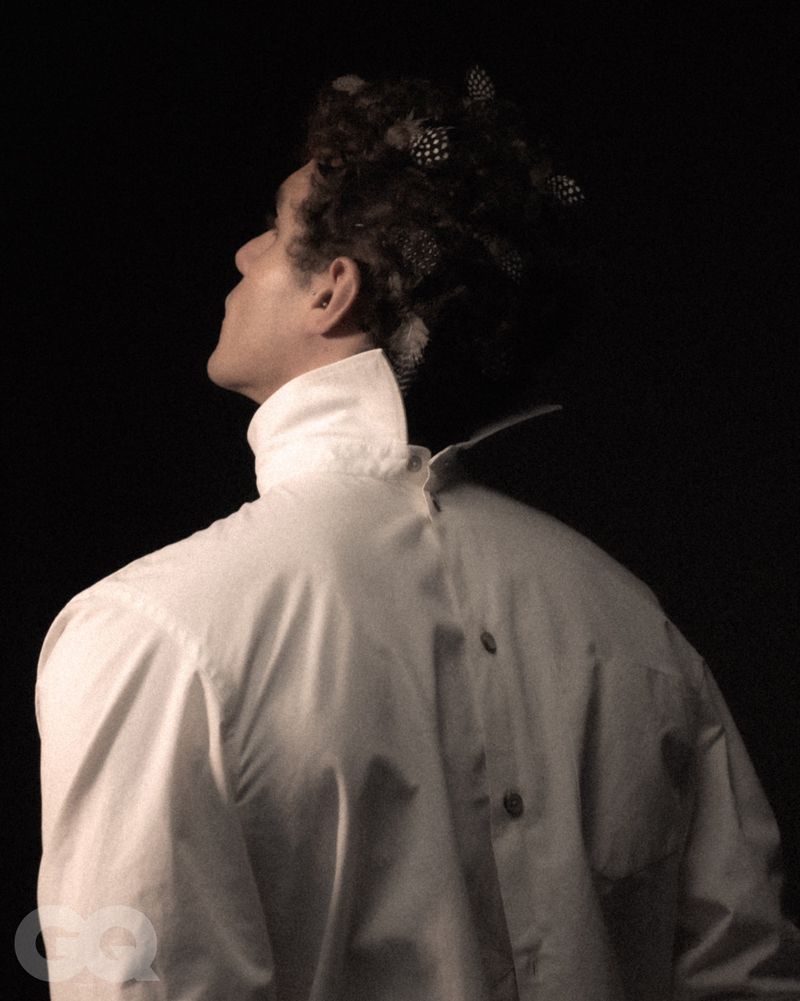 Man wearing a backwards white button-down shirt with feathered hair against a dark background