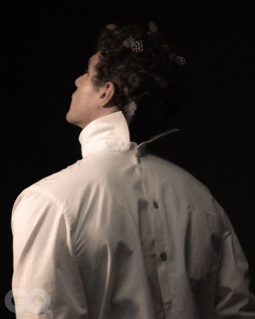Man wearing a backwards white button-down shirt with feathered hair against a dark background