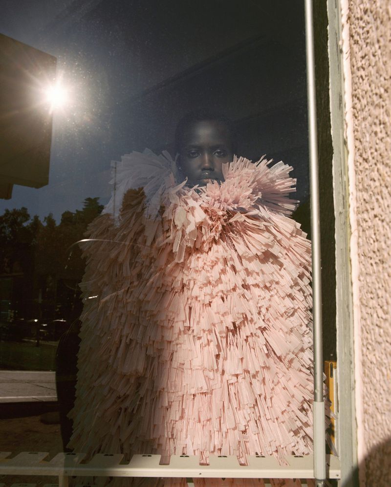 Model Yar Aguer in a textured pink fringed garment viewed through a glass window for Vogue Espana photography by Pablo Zamora.