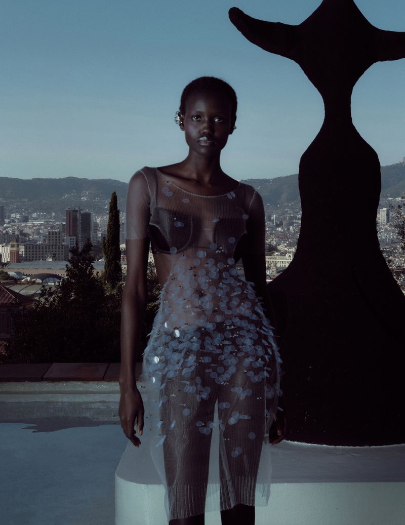 Model Yar Aguer in a sheer embellished dress standing on a rooftop with a city skyline background for Vogue Espana.