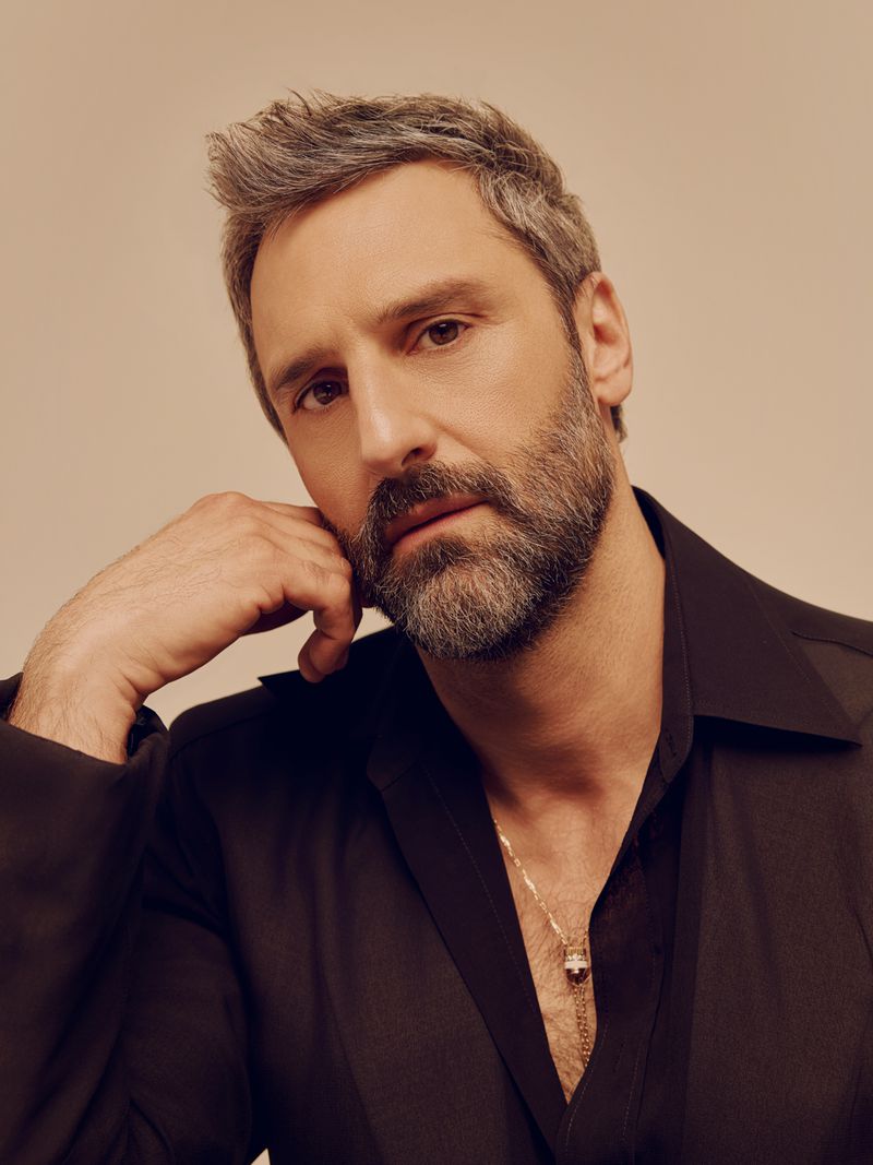 Portrait of Marco Calvani wearing a black shirt with a gold chain necklace against a neutral background