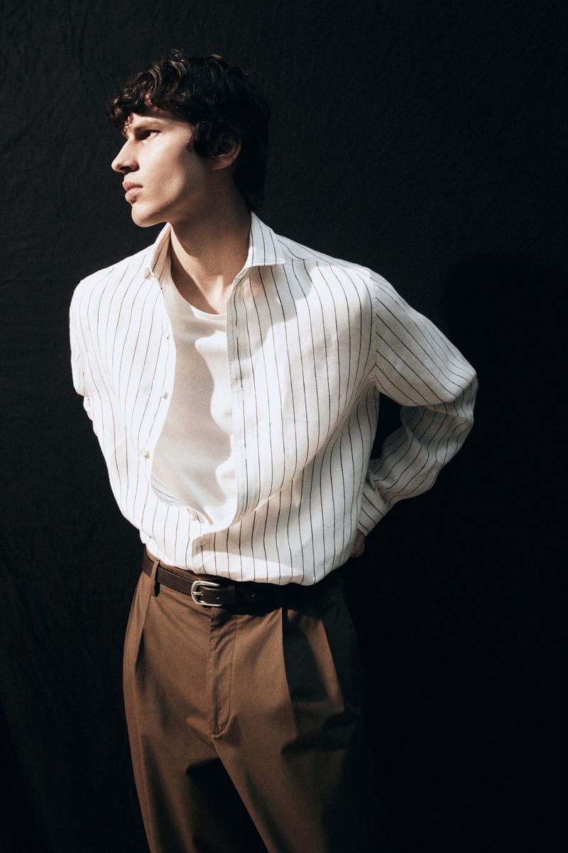 Male model wearing a striped shirt and brown trousers against a dark background for Massimo Dutti