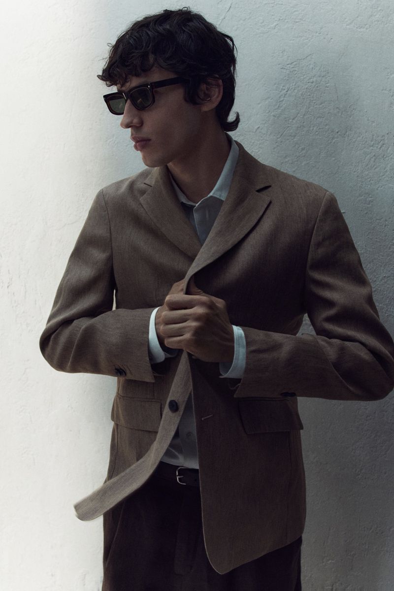 Model in dark sunglasses wearing a brown blazer against a textured white wall for Massimo Dutti Summer Looks.