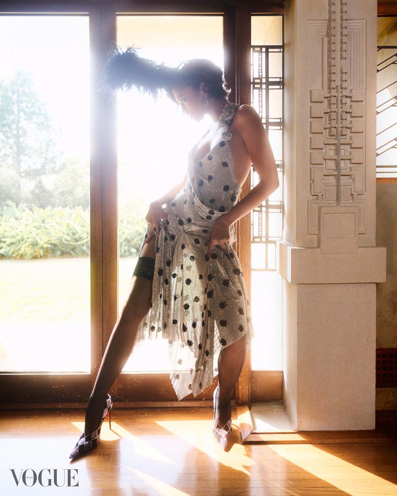 Zendaya posing by a window in a polka dot dress with feathered headpiece for Vogue Brasil, photographed by Nicole Heiniger