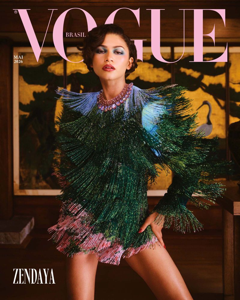 Zendaya posing for Vogue Brasil cover wearing a heavily fringed green and blue textured dress against a dark interior setting