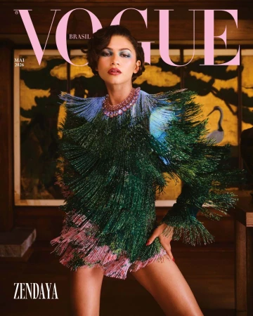Zendaya posing for Vogue Brasil cover wearing a heavily fringed green and blue textured dress against a dark interior setting