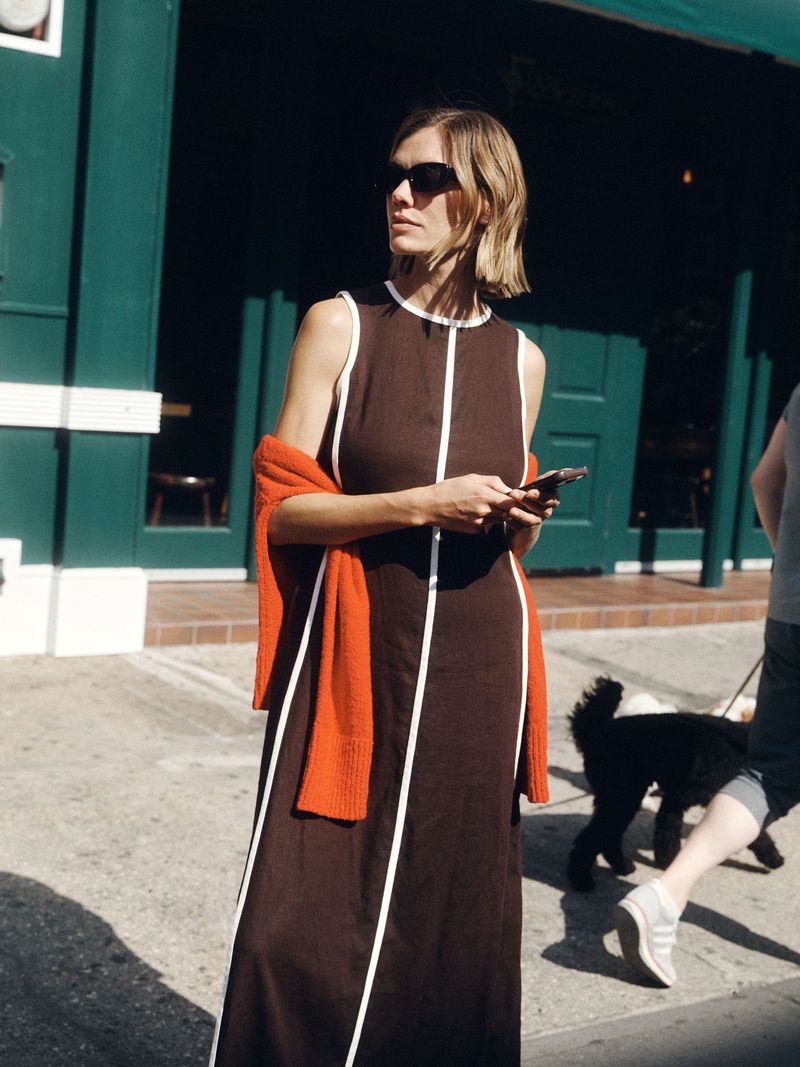 Model Joanna Halpin in a brown and white piped maxi dress holding a phone outdoors for ME+EM