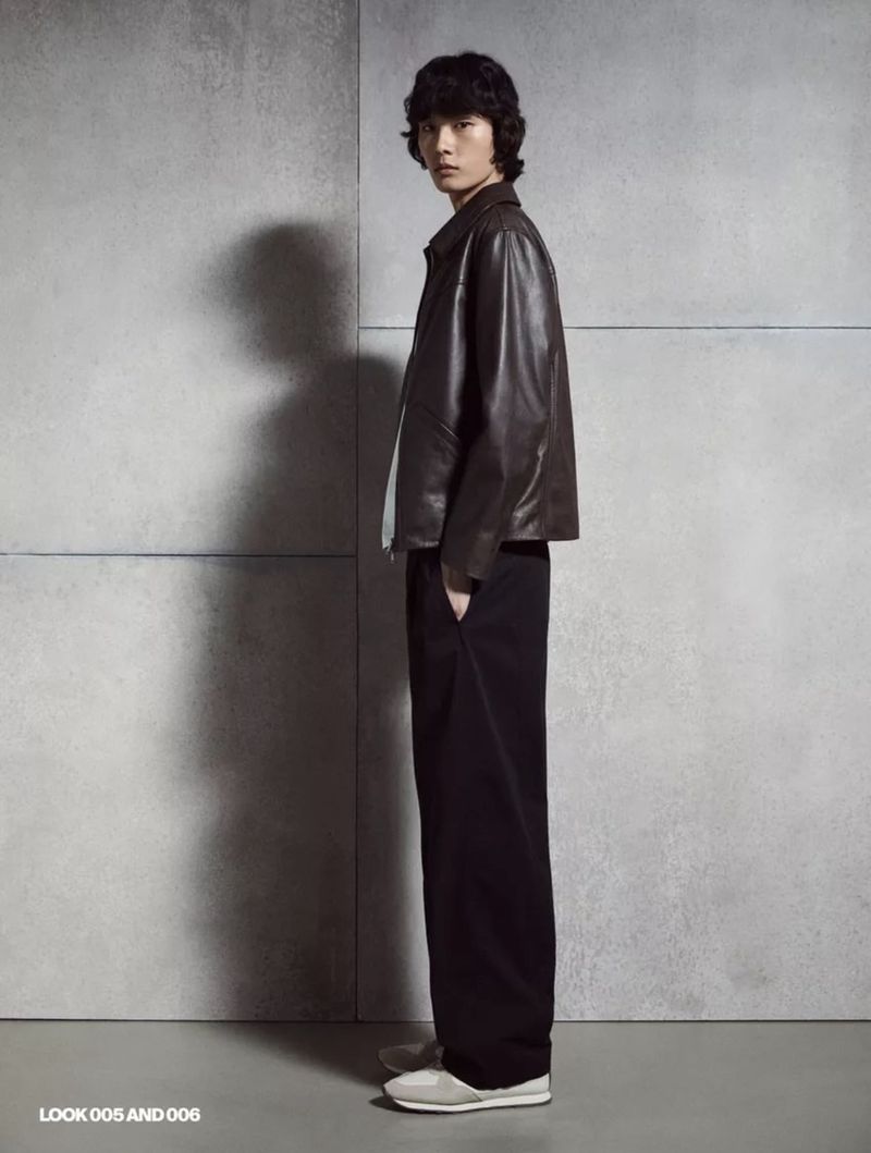 Model standing against a grey concrete wall wearing a dark brown leather jacket and black trousers for Massimo Dutti