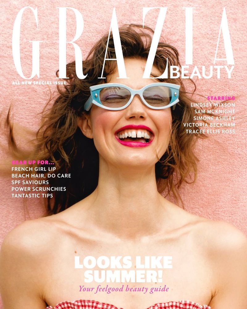 Magazine cover featuring a smiling adult woman with sunglasses, bright pink lipstick, and wavy hair, against a pink background.