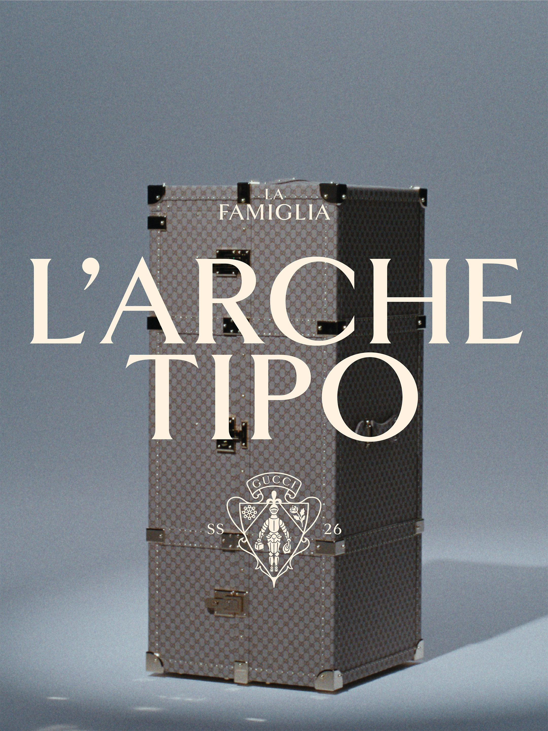 Large monogram trunk displayed against a muted grey background with elegant white serif typography