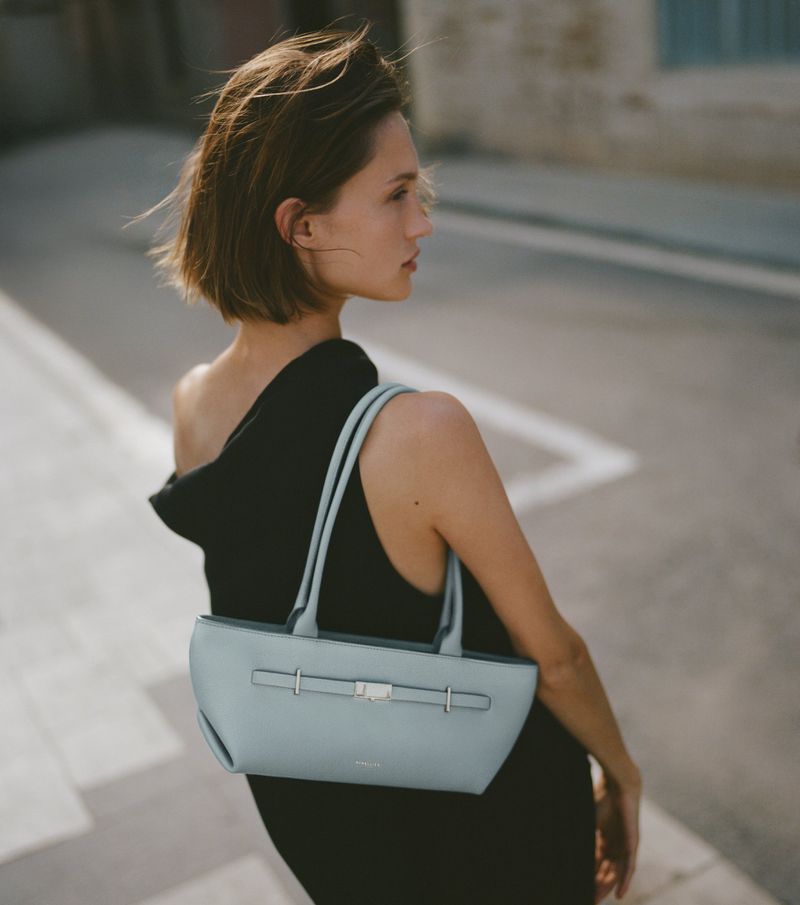 Model wearing a black top holding a light blue shoulder bag outdoors on a street