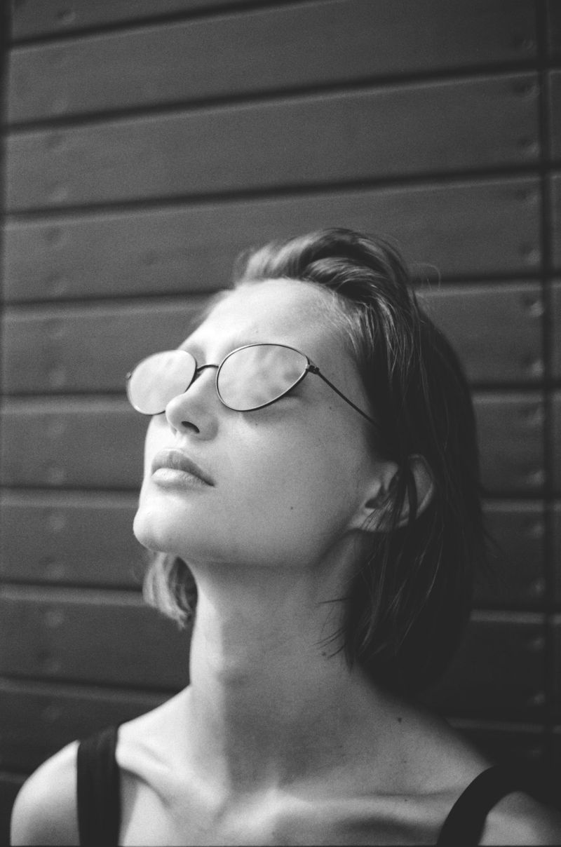 Monochrome portrait of a model wearing dark sunglasses with reflective lenses against horizontal wood slats.