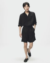 Asian man walking forward in a black shirt, black shorts, and black shoes against a plain white seamless background.