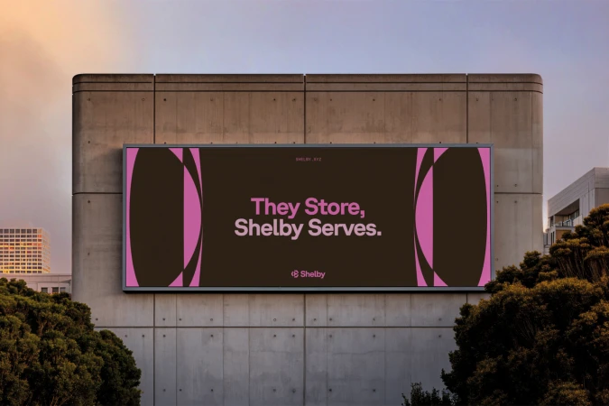 Large outdoor advertising billboard on a concrete building exterior displaying branding with pink typography against a dark brown background.