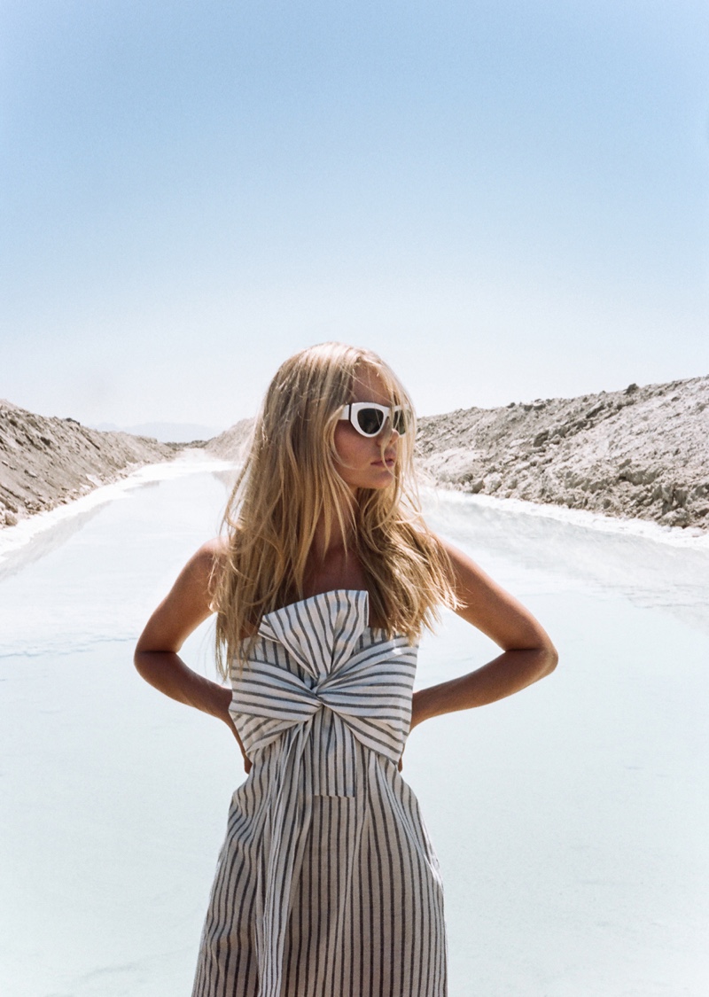 Woman in striped dress and sunglasses poses on salt flat under a blue sky. Fashion photography in a natural environment.