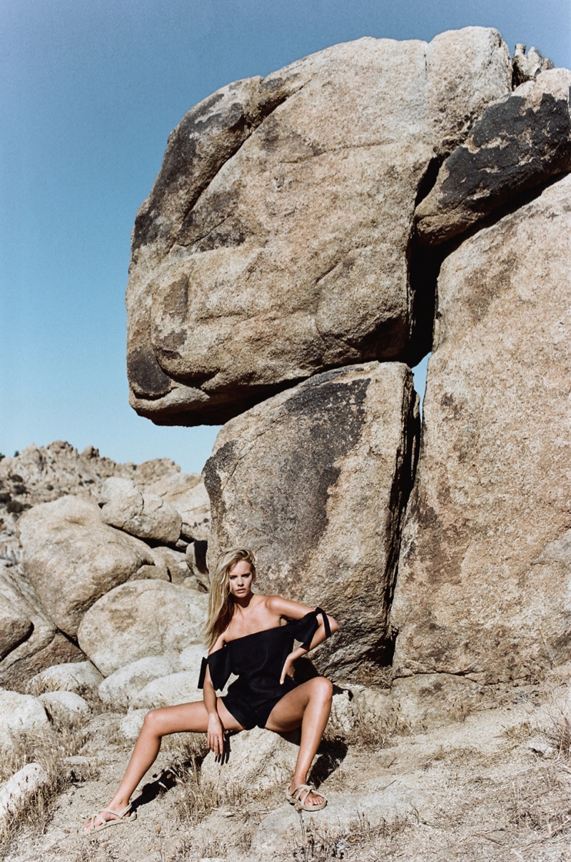 Model Marloes Horst wearing a black off-the-shoulder outfit posing amongst large desert rocks under a clear blue sky.