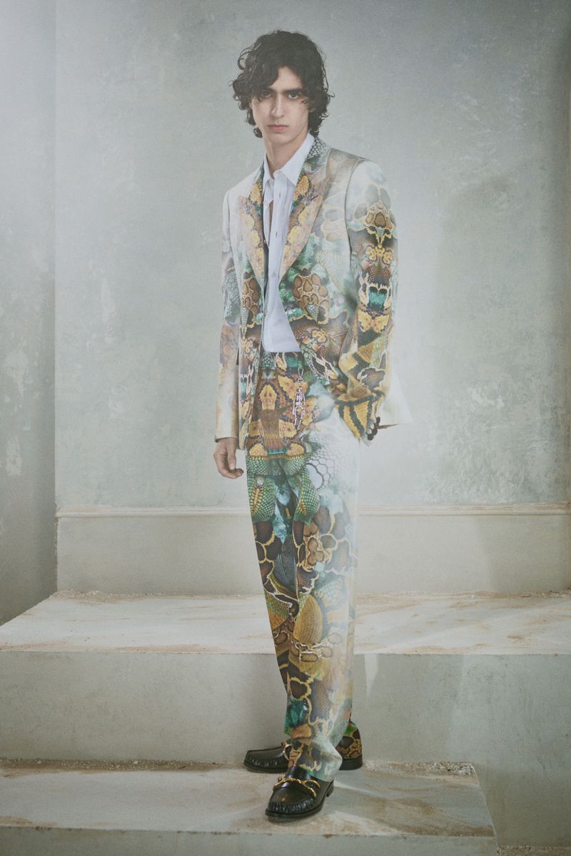 Model wearing a patterned printed suit standing on concrete steps against a textured grey wall