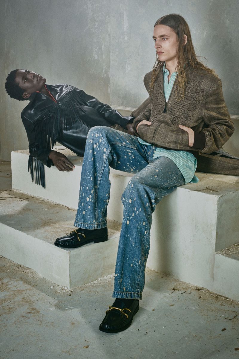 Two male models posing on tiered white concrete platforms against a mottled grey wall in Alexander McQueen menswear