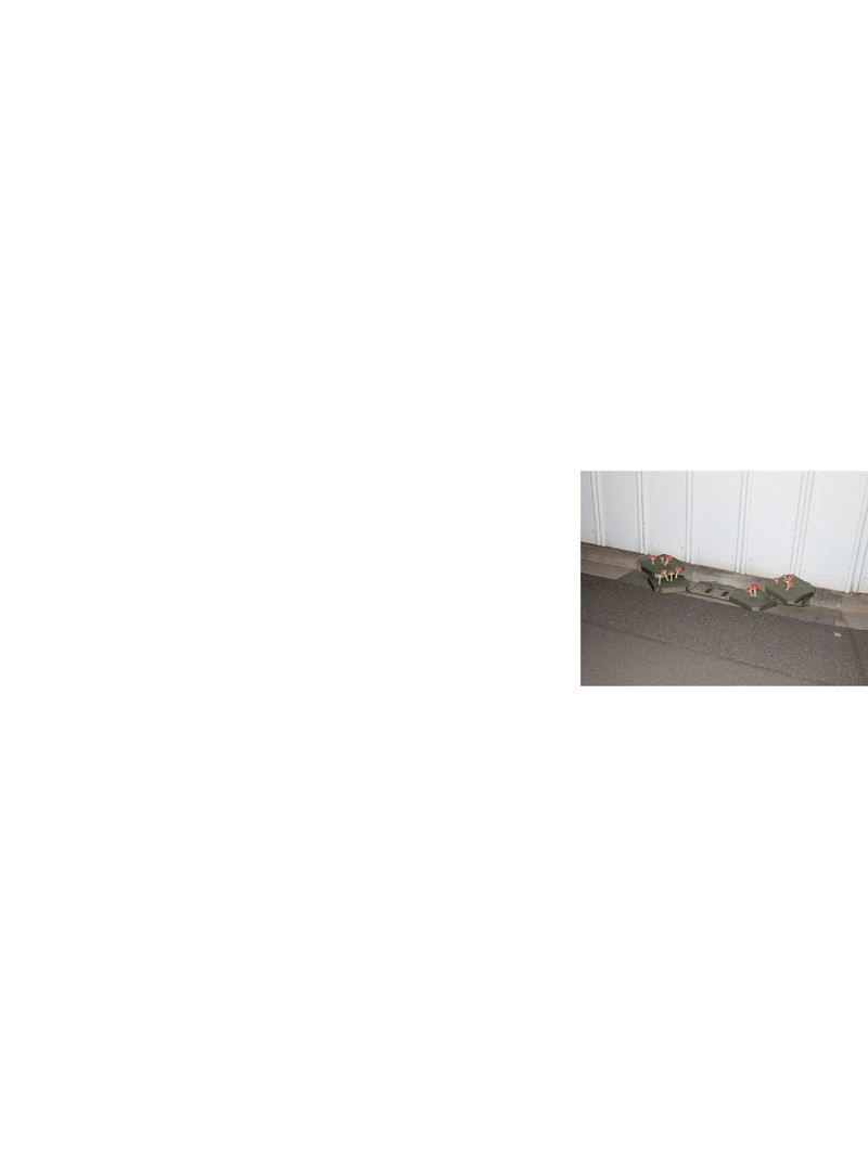 Two pairs of camouflage military boots sit indoors against a textured white wall on a gray floor in a medium, naturally lit shot.