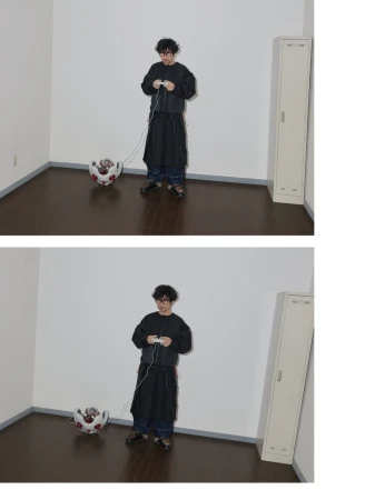 Adult wears glasses, a black jacket, and dark pants, playing a video game with a wired controller, indoors with a unique teapot-like object.