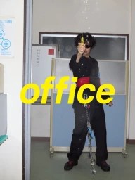 Man wearing a black outfit and red belt holding a water pistol in an office setting with large yellow text overlaid.