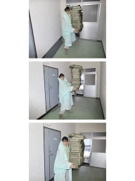 Person wearing mint green coat and glasses carrying a towering stack of cardboard boxes in a hallway for Office Magazine