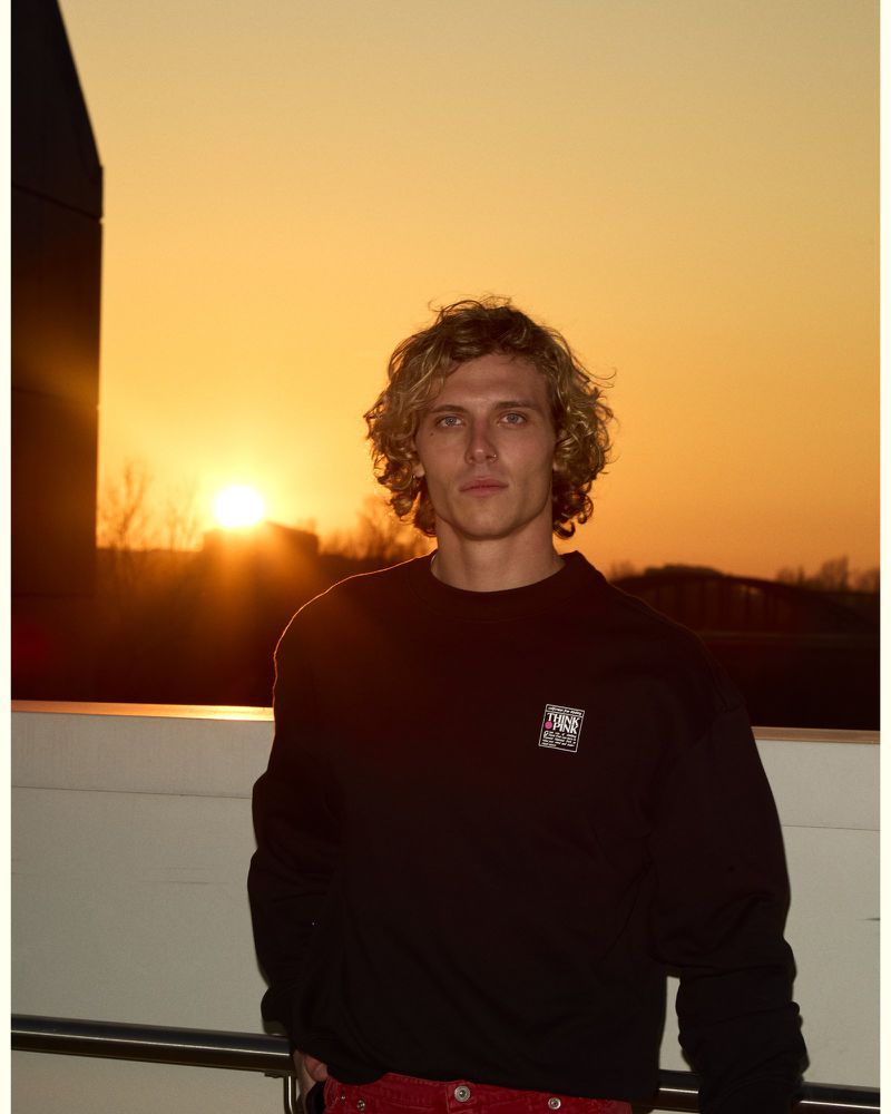 Young man with curly blonde hair wearing a black sweatshirt standing outdoors during a golden sunset.