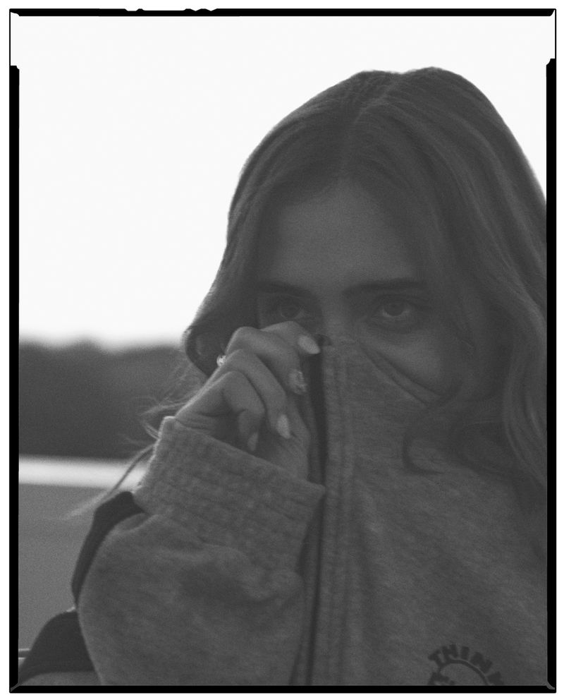 Black and white portrait of a woman pulling her grey hoodie up to cover her lower face.