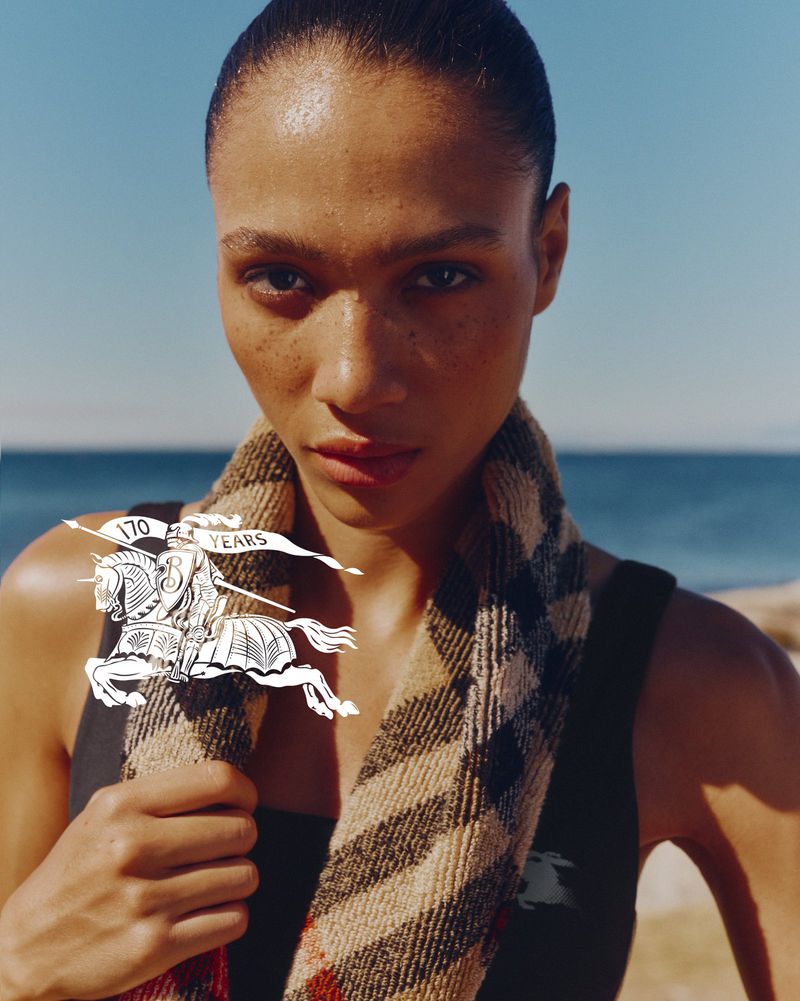 Close-up portrait of a model wearing a plaid scarf outdoors with an ocean and sky background for Burberry Athleisure